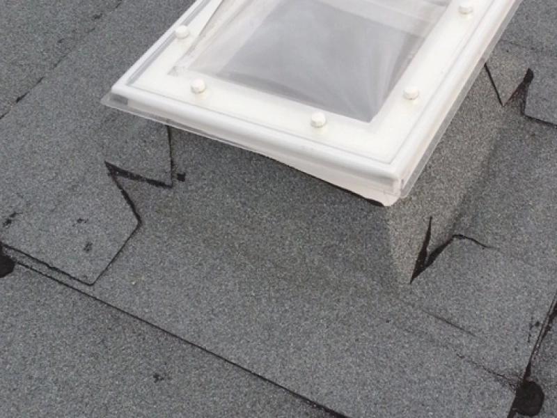 Rechteckige Lichtkuppel auf einem Bitumen-Flachdach, die Dachbahn ist rundherum aufgeschnitten und hochgestellt.