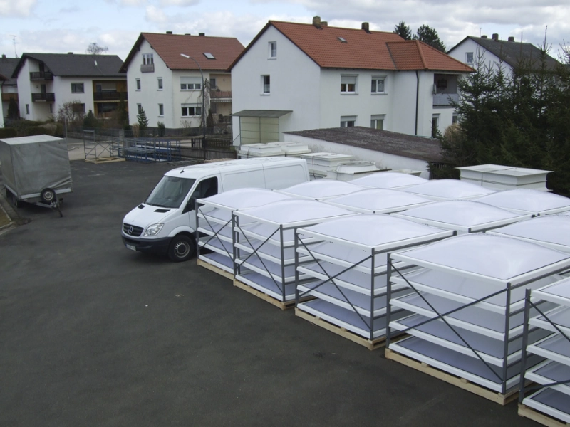 Hof mit Transportgestellen voller Lichtkuppeln, davor ein Transporter und ein Planenanh&auml;nger.