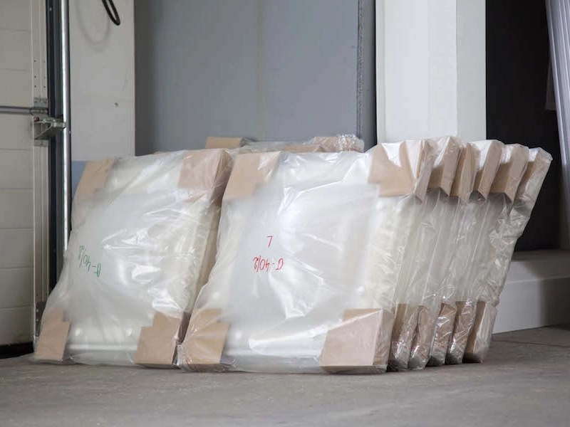 Folienverpackte Kuppelschalen mit Eckschutz stehen aufgereiht im Hallentor, handschriftlich beschriftet.