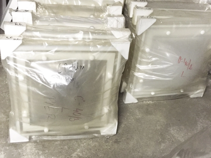 Folienverpackte Kuppelschalen mit Eckschutz vor einer Palette, mit roter und schwarzer Schrift beschriftet.