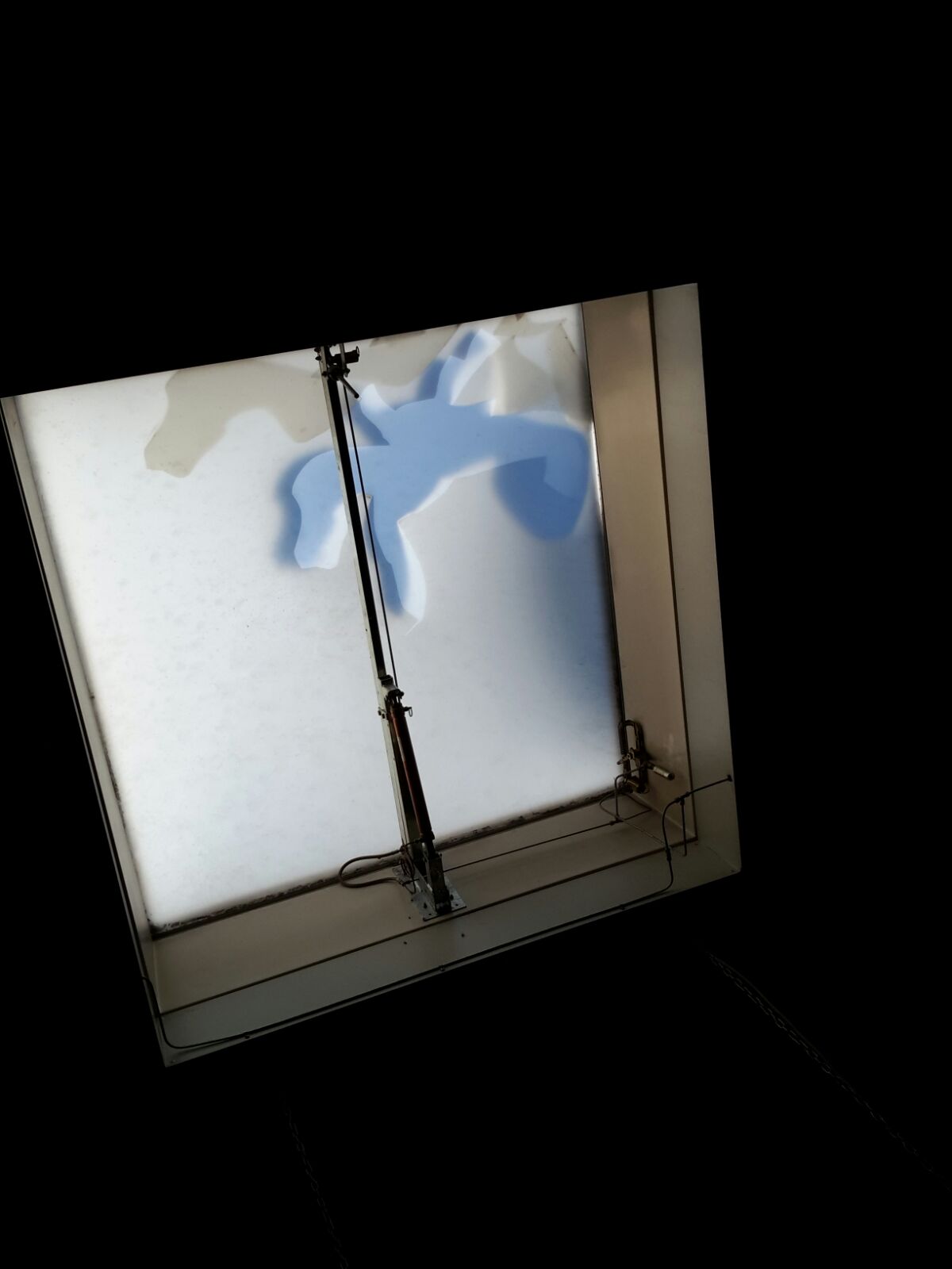 Blick von unten auf eine geschlossene Lichtkuppel: milchig durchscheinende Schale, in der Mitte ein Spindelantrieb zum Öffnen, daneben verlegte Kabel.