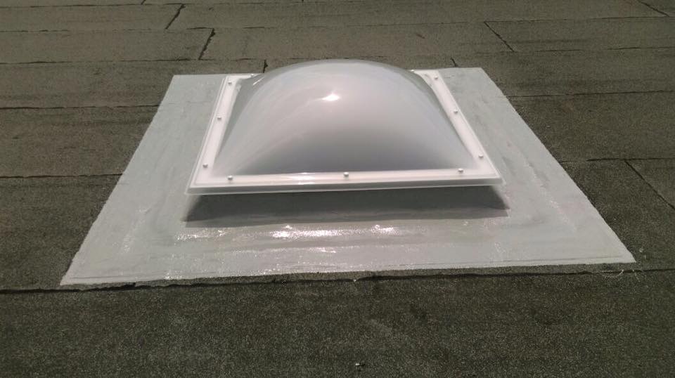 Runde Lichtkuppel auf einem Bitumendach, der Aufsatzkranz ist mit grauer Flüssigfolie eingedichtet.