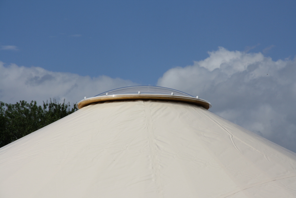 Nahaufnahme der runden Lichtkuppel auf der Spitze einer Jurte vor blauem Himmel.