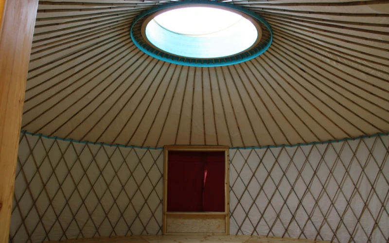 Blick in eine Jurte: das Holzgitter der Wand, das Speichenrad der Decke und in der Mitte eine runde Lichtkuppel.