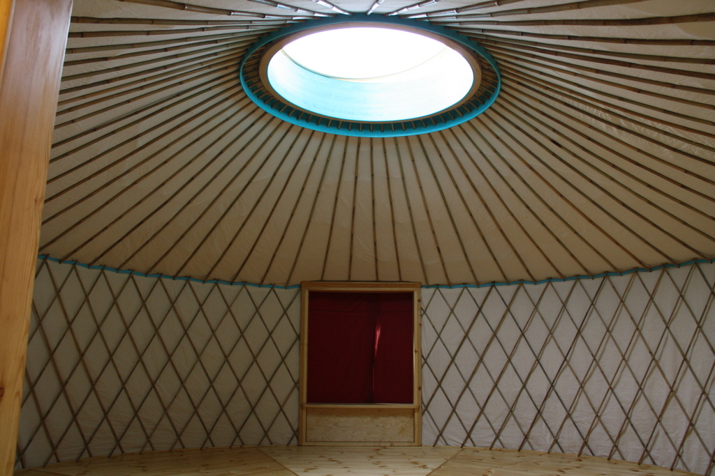 Blick in eine Jurte: das Holzgitter der Wand, das Speichenrad der Decke und in der Mitte eine runde Lichtkuppel.