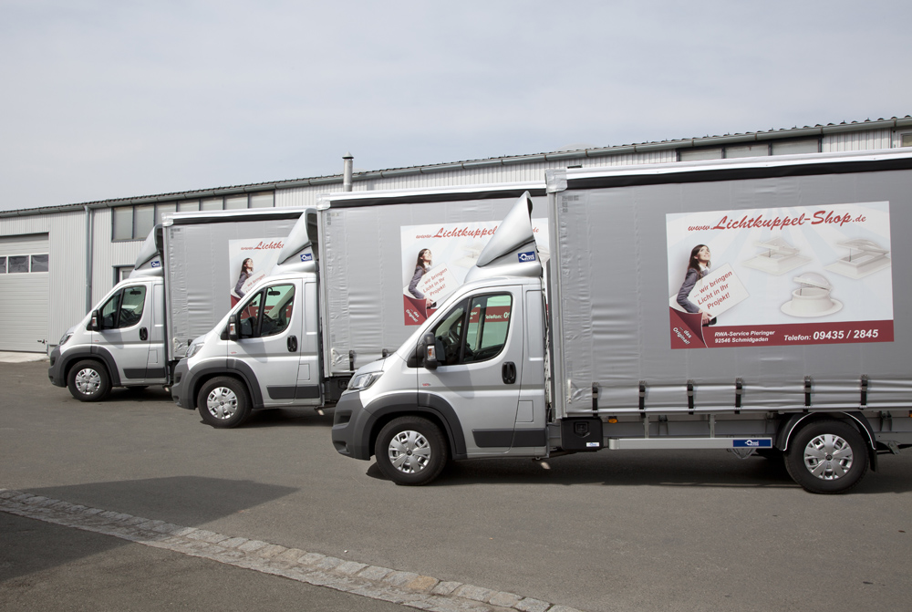 Drei silberne Lastwagen mit Planenaufbau vor einer Halle, auf der Plane die Aufschrift www.Lichtkuppel-Shop.de.