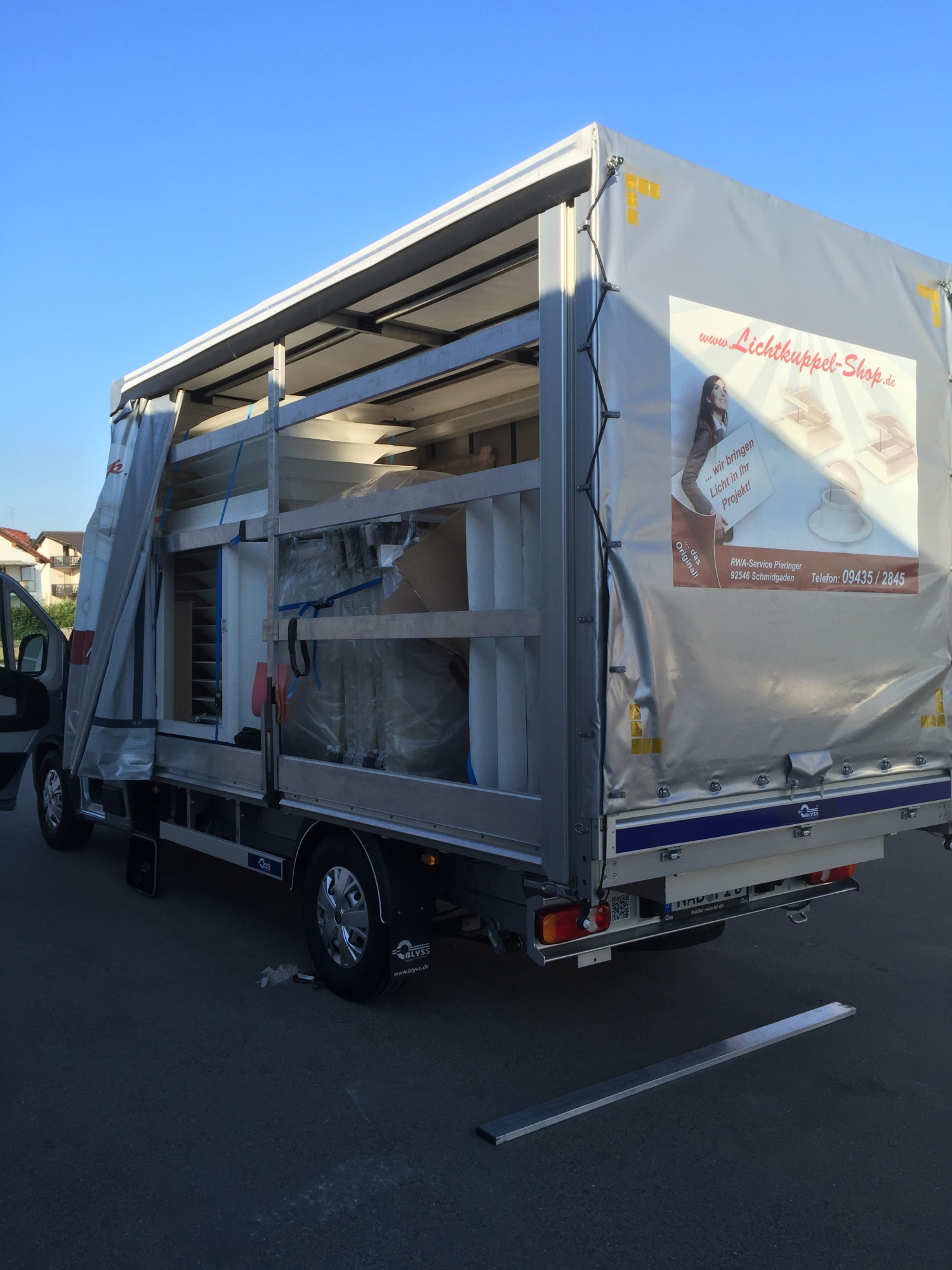 Lastwagen mit geöffneter Plane, darin verpackte Lichtkuppeln und Aufsatzkränze, auf der Plane die Aufschrift www.Lichtkuppel-Shop.de, RWA-Service Pieringer, 92546 Schmidgaden.