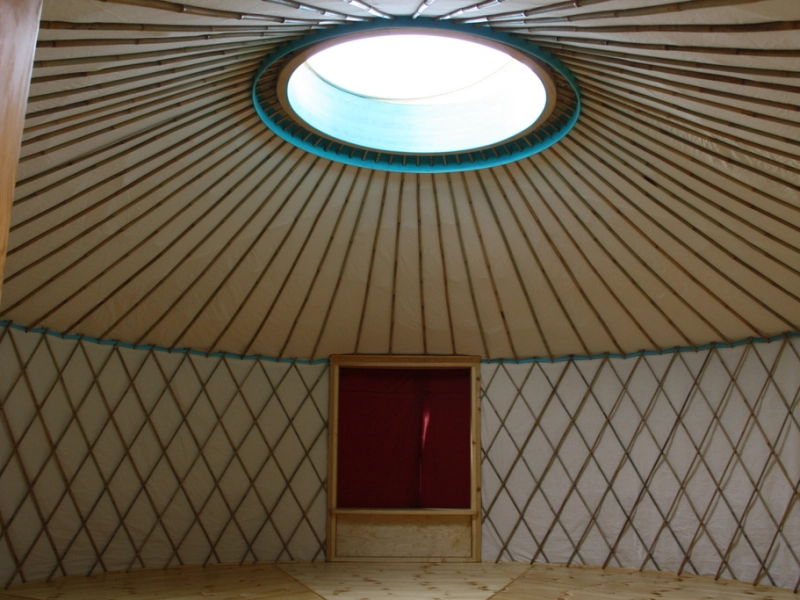 Blick in eine Jurte: das Holzgitter der Wand, das Speichenrad der Decke und in der Mitte eine runde Lichtkuppel.