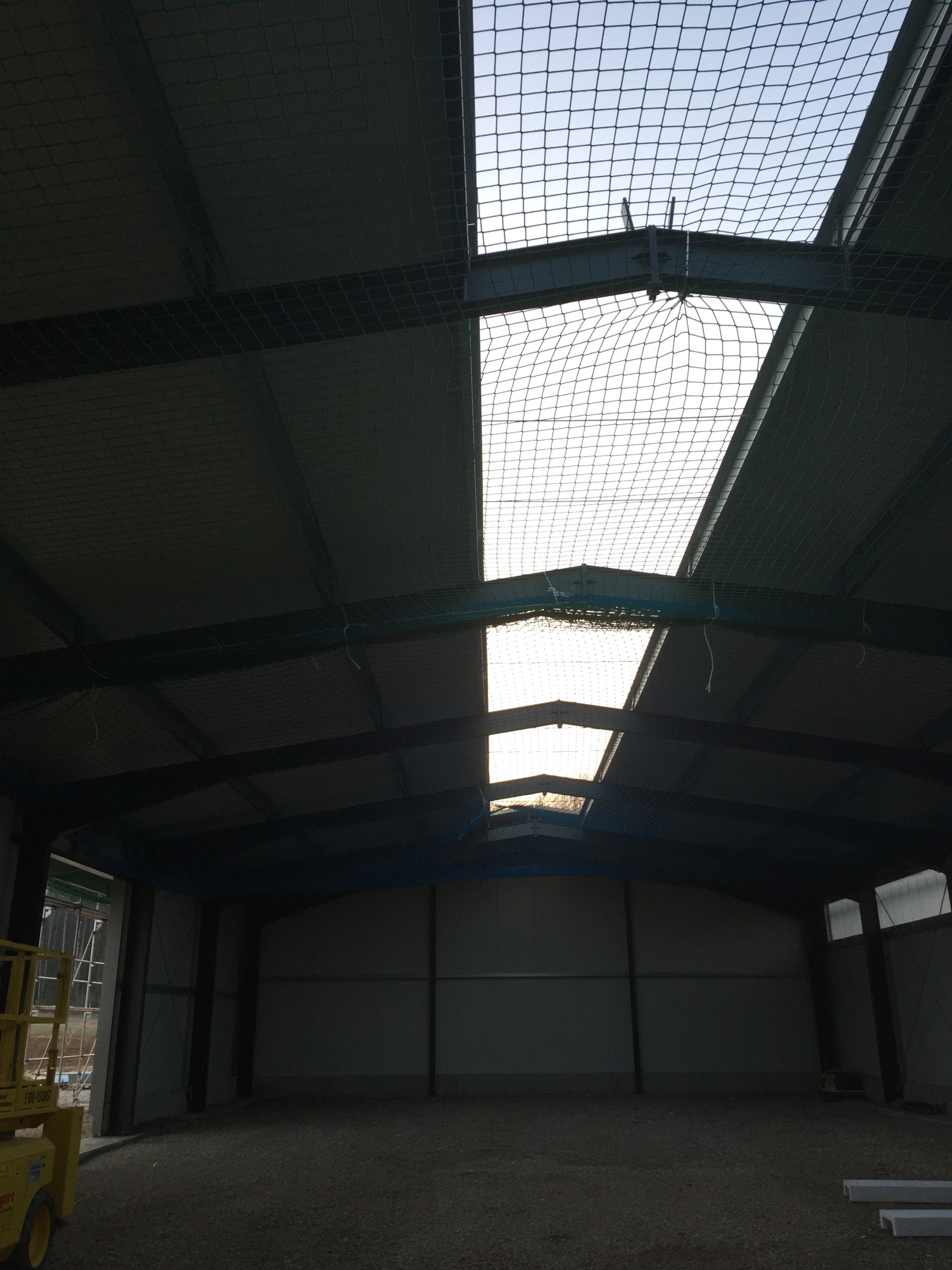 Blick von innen in die Halle: Durch das Firstlichtband fällt Tageslicht auf die noch leere Bodenfläche, darunter hängt ein grünes Sicherungsnetz.