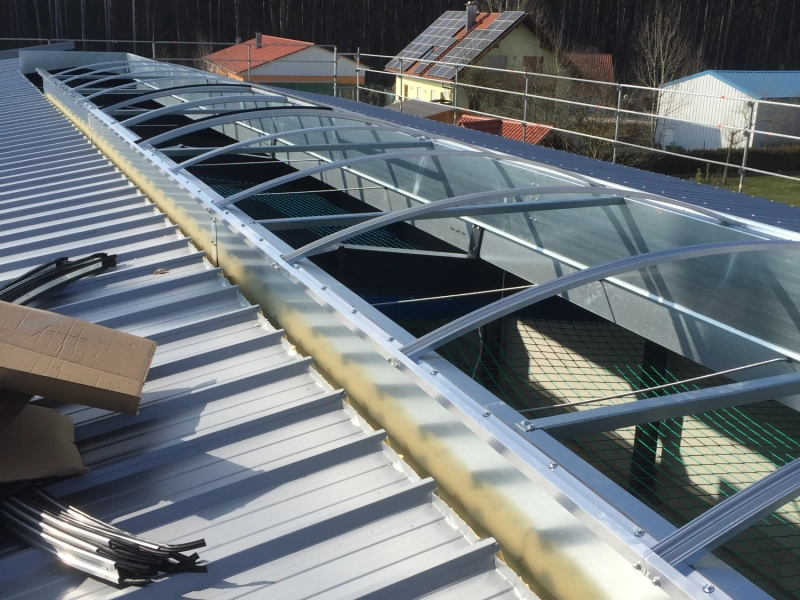 Der Aluminiumbogen des Lichtbands mit eingeschobenen Stegplatten, links auf dem Trapezblech liegen Dichtprofile und Kartonage.