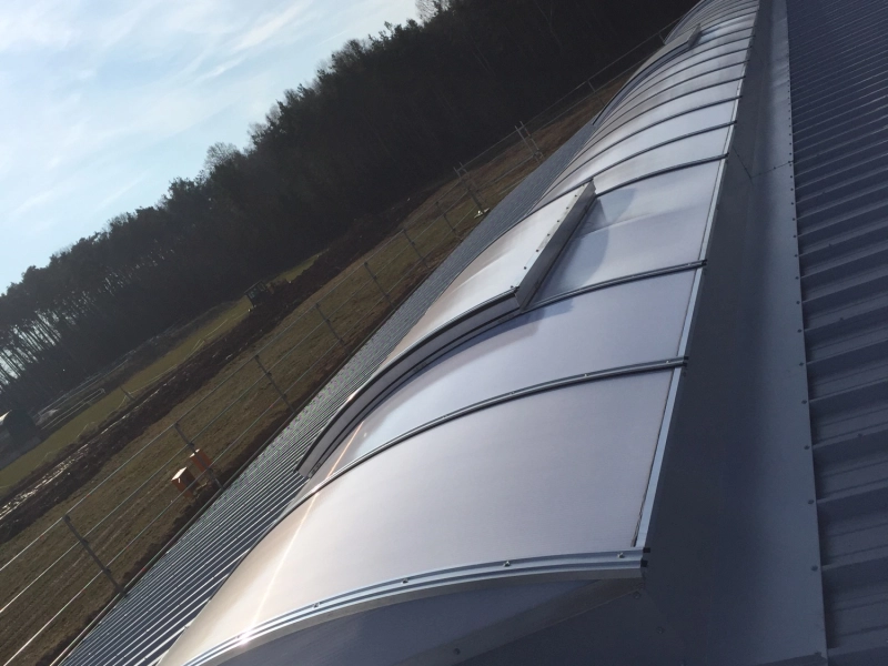 Das fertige Lichtband aus der Untersicht entlang der Dachkante, dahinter Feld und Waldrand.