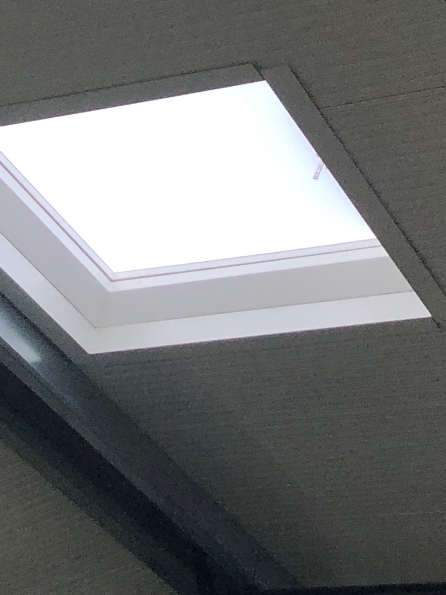 Nahaufnahme von unten: die quadratische Lichtöffnung mit weißer Laibung in der grauen Sandwich-Decke.