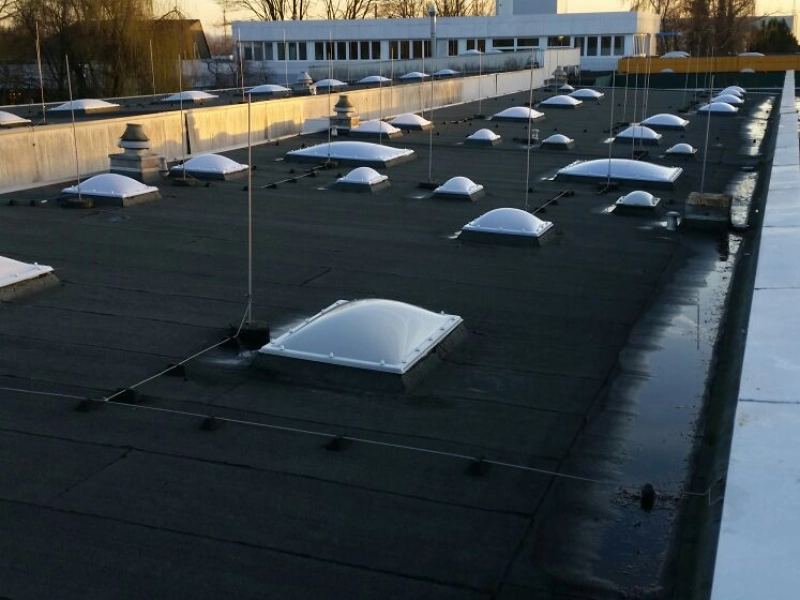 Dachfl&auml;che mit zahlreichen neuen Lichtkuppeln in Reihen, dahinter ein B&uuml;rotrakt, am Himmel Kondensstreifen.
