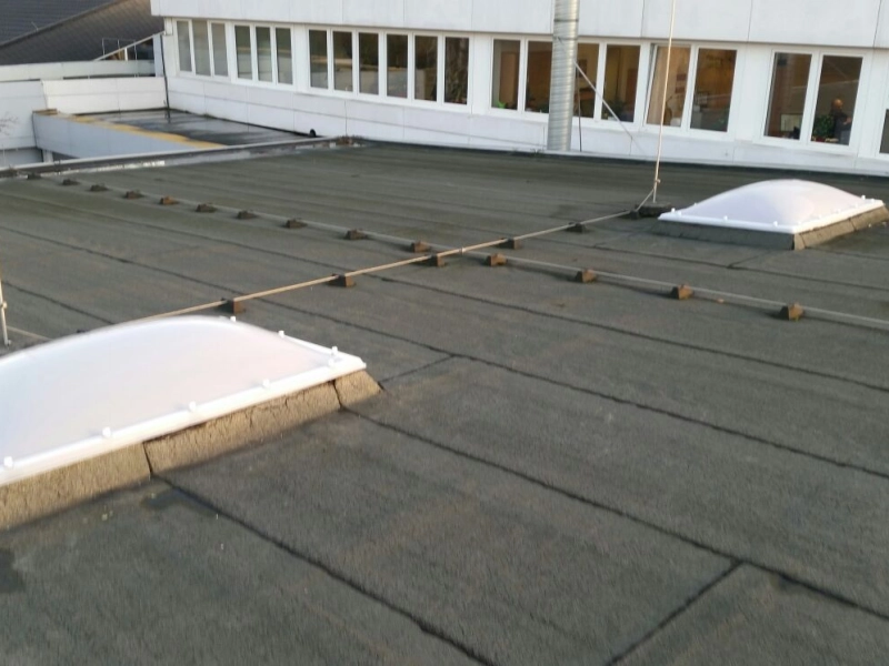 Zwei neue Lichtkuppeln auf Betonkr&auml;nzen, dazwischen ein gespanntes Sicherungsseil, dahinter ein B&uuml;rogeb&auml;ude mit Fensterband.