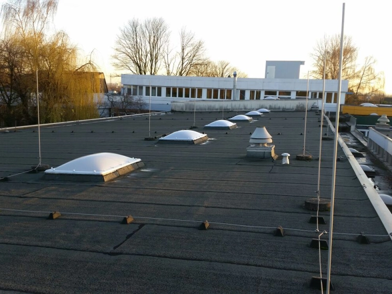 Weite Dachfl&auml;che mit Lichtkuppeln und mehreren L&uuml;ftungshauben, dahinter ein Flachbau im Licht der tiefstehenden Sonne.