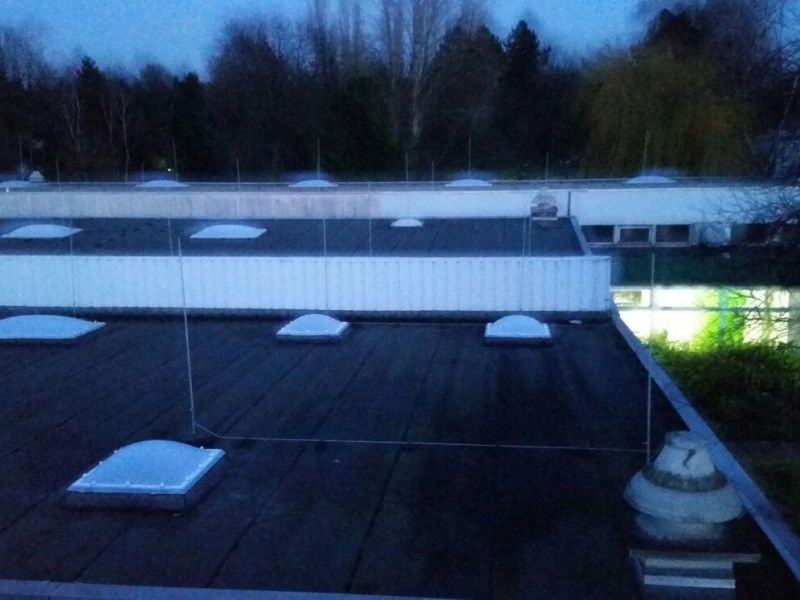 Dachfl&auml;chen mit Lichtkuppeln in der D&auml;mmerung, rechts die erleuchteten Fenster eines B&uuml;rotrakts.