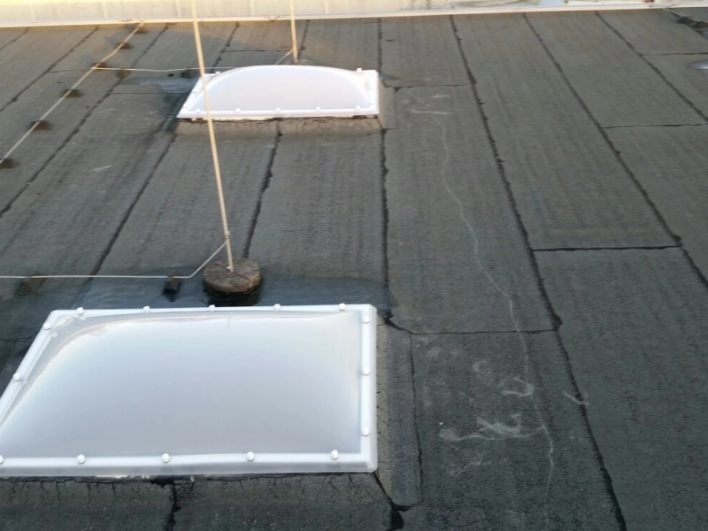Zwei neue Lichtkuppeln auf der Bitumendachfl&auml;che, dazwischen Sicherungsseile und Haltestangen.