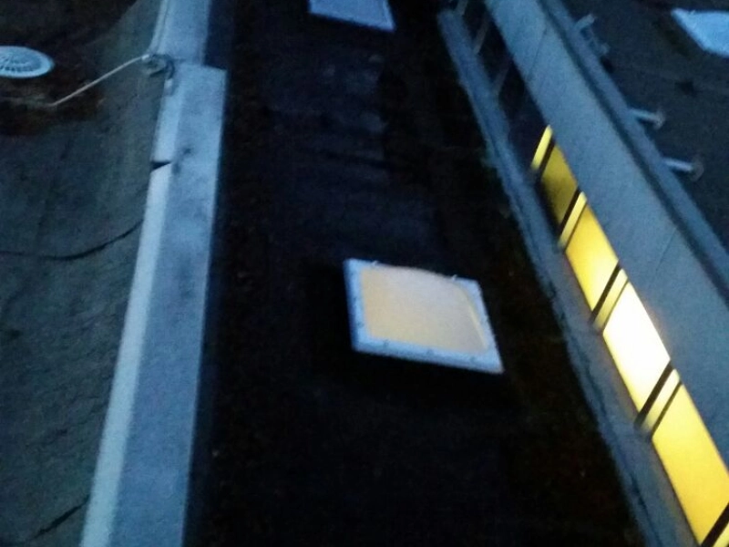 Steiler Blick in einen schmalen Dachbereich zwischen zwei Geb&auml;udeteilen mit einem von innen beleuchteten Oberlicht, rechts eine gelb erleuchtete Fensterreihe.