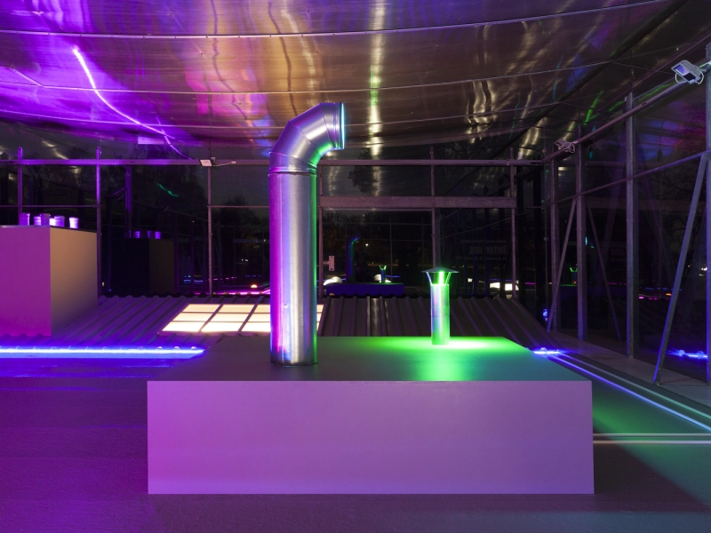 Blick auf ein Podest mit senkrechtem L&uuml;ftungsrohr, dar&uuml;ber die violett angestrahlte Deckenfolie des Pavillons.