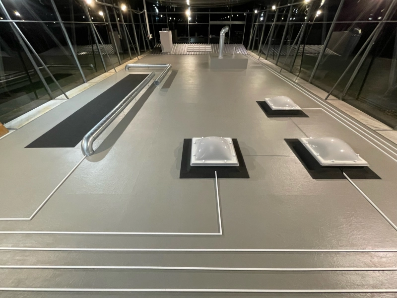 Dieselbe Installation bei heller Beleuchtung: graue Bodenfl&auml;che mit drei Lichtkuppeln auf schwarzen Unterlagen und verlegten Rohren.